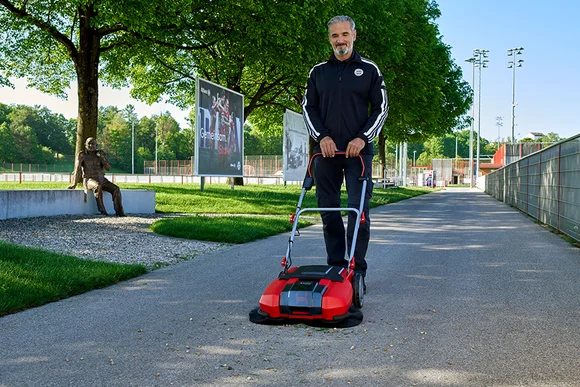 Person reinigt Weg mit Kehrmaschine